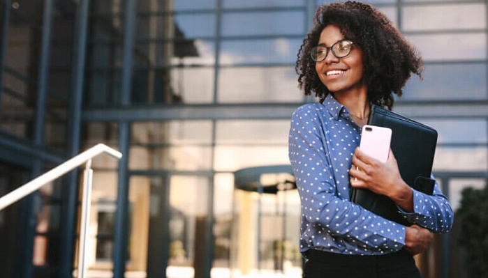 Worker with laptop and cell phone in front of her office smiling